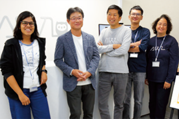北出氏（右から3番目）と川村教授（右から4番目）を中心に、グローバルに活躍する外国人スタッフたち。多様な文化と視点を持つ人材が、AI開発と技術革新の基盤を支えている